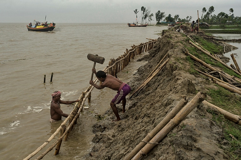 Land of high tide, men working to drive in posts to retain soil embankment on the coast from erosion by high tides